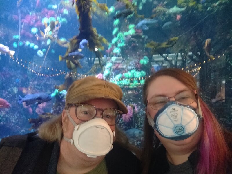 Holly and James selfie in front of the aquarium in the international terminal full of brightly colored fish. Both are masked
