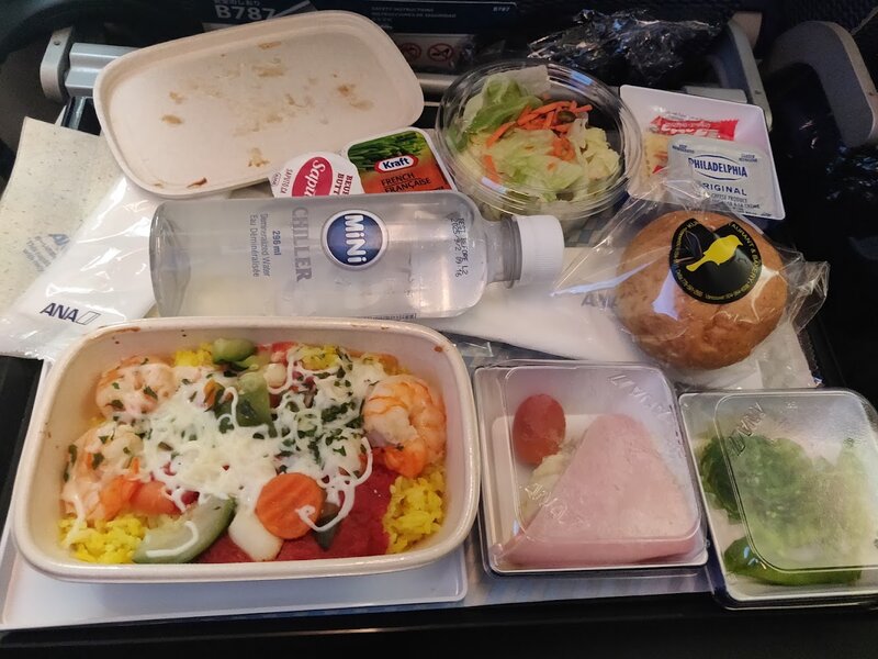 Airplane meal with shrimp on rice, salad, gomae, ham and something, and metal cutlery