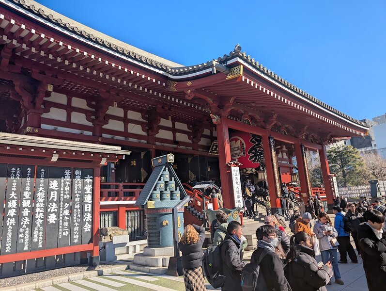 Closer view of the temple, with an old metal bell, stairs leading into the temple itself, and a large red paper lantern.