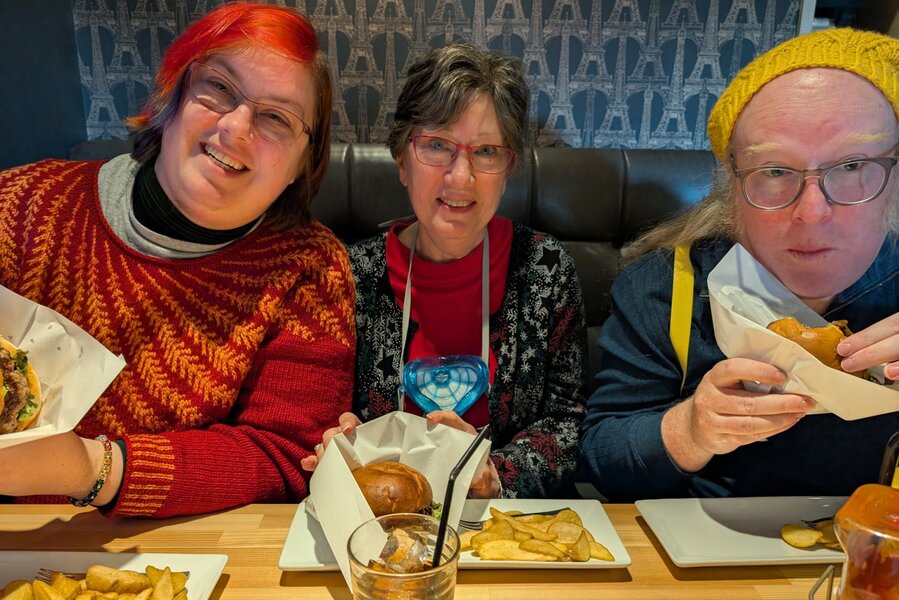 Group shot of me, Mom and James. I have my burger in my hand, mom is displaying hers on her plate, and James has already taken a bite. The burgers look thick and juciy, with wedge cut fries as a side.