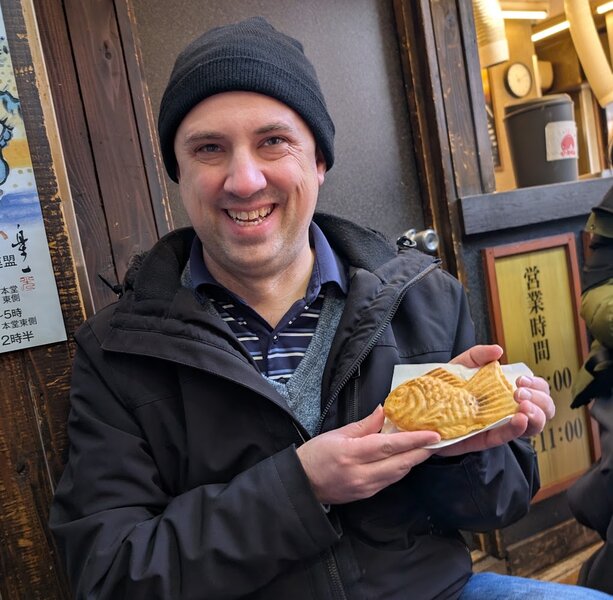 Andrew smiling holding a fresh taiyaki, a waffle shaped like a fish