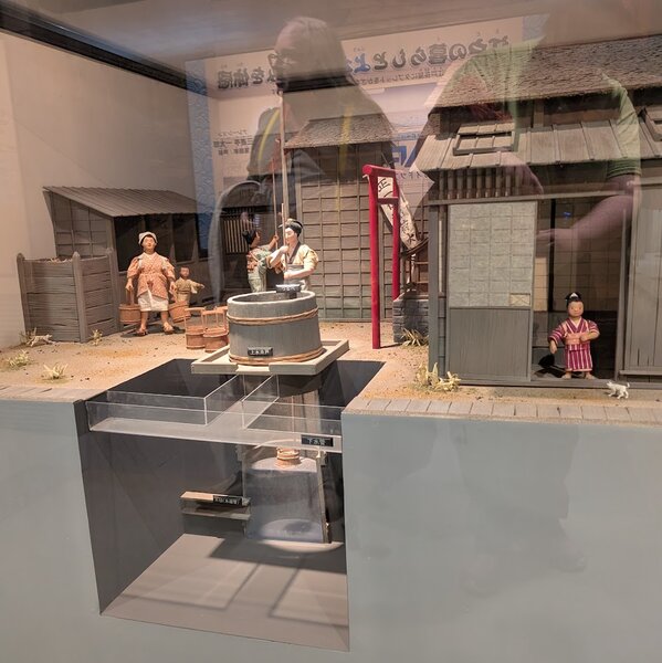 Diorama of a village well, with a cutaway showing the fresh water coming to the well and the dirty water leaving via an different path